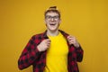 confident guy in glasses with curly hair puts on a shirt on a yellow background