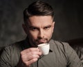 Confident handsome bearded man with cup of coffee sitting on comfortable leather sofa on dark background. Royalty Free Stock Photo