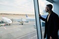 Confident handsome businessman on a business trip stands at the panoramic window in the waiting room of the international airport Royalty Free Stock Photo