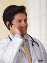 Confident handsome doctor with an Stethoscope around his neck, using a celphone with one hand, in office background Royalty Free Stock Photo