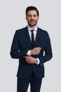 Confident and handsome. Good looking young man in full suit adjusting sleeve and looking at camera with smile while standing Royalty Free Stock Photo