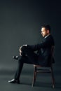 Confident handsome man in black suit sitting on the chair on dark backround