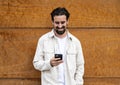 Confident handsome young guy leaning against a wooden wall while texting with his phone. Happy and relaxed man using his Royalty Free Stock Photo
