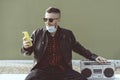 Confident hipster man video calling against green wall background while listening music with a vintage boombox player - Man with