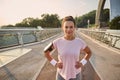 Confident Hispanic sportswoman, female athlete, runner in pink t-shirt, wearing smartphone holder and earphones, smiles looking at