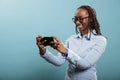 Confident joyful young adult with mobile cellphone browsing webpage on blue background.