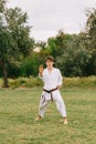 Confident karate boy in white kimono on a park background. Outdoors exercises concept. Copy space.