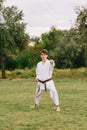 Confident karate boy in white kimono on a park background. Outdoors exercises concept. Copy space.