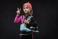 Confident little skater girl dressed in sportswear holds ice skates and shows victory hand. Isolated on a dark textured Royalty Free Stock Photo