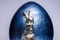 Confident looking easter bunny figure in front of a royal blue easter egg on a white and uniform background, easter decoration