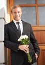 Confident in love. Portrait of a handsome man leaning against a wall holding a bunch of white roses and smiling. Royalty Free Stock Photo