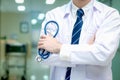 Confident male doctor in white workwear holding stethoscope standing with arms crossed in corridor of medical clinic, doctor Royalty Free Stock Photo