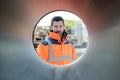 Confident male engineer looking through large pipe at construction site