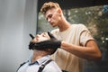 A beautiful male sitting in a barber chair and shaved by a barber on a beauty salon background. Barbershop concept.