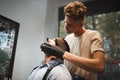 A beautiful male sitting in a barber chair and shaved by a barber on a beauty salon background. Barbershop concept.