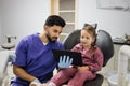 Confident male smiling professional dentist showing tablet pc computer to happy kid patient Royalty Free Stock Photo