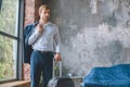 confident male traveler with jacket over shoulder standing with suitcase in bedroom