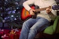 Confident male in warm clothes holding music instrument in hands on Christmas tree background Royalty Free Stock Photo