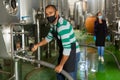 Confident male winegrower working in cellar, filtering wine in barrels