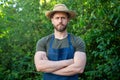 Confident man gardener in gardening apron and farmers hat keeping arms crossed standing in garden Royalty Free Stock Photo