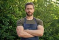 Confident man gardener in gardening apron keeping arms crossed standing in garden outdoors Royalty Free Stock Photo