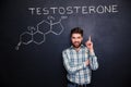 Confident man pointing on chemical structure of testosterone at chalkboard