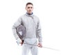 Confident man professional fencer standing with helmet and rapier on white