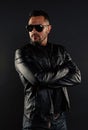Confident man stand with arms folded. Bearded man in trendy sunglasses. Fashion model in leather jacket and jeans Royalty Free Stock Photo