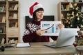 Confident mature adult businesswoman in Santa hat pointing at graphic materials