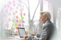 Confident mature businesswoman using laptop while sitting with document at desk in office Royalty Free Stock Photo