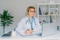 Confident mature caucasian senior female doctor in white coat using laptop for telemedicine with patients at hospital Royalty Free Stock Photo