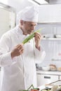 Confident mature chef smelling fresh scallion bunch while standing at restaurant kitchen