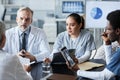 Confident mature doctor and his young female assistant looking at colleague Royalty Free Stock Photo