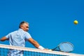 Low angle view of confident mature man hitting tennis ball with racket on court against clear blue sky Royalty Free Stock Photo