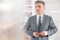 Confident mature salesman looking away while buttoning suit against wall in apartment