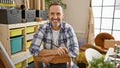 Confident mid-aged artist, grey-haired man, smiling and relaxed while sitting with arms crossed in a vibrant art studio Royalty Free Stock Photo