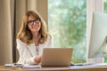 Confident mid aged business woman sitting at desk and using laptop for work