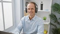 Confident middle age man, a smiling business worker, using laptop and headphones working on his job at the office, managing online Royalty Free Stock Photo