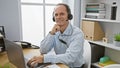 Confident middle age man, a smiling business worker, using laptop and headphones working on his job at the office, managing online Royalty Free Stock Photo