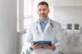 Confident middle aged male doctor in uniform holding clipboard and looking at camera, therapist man standing in clinic Royalty Free Stock Photo