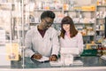 Confident multiethnical Male And Female Pharmacists In Pharmacy. African American man pharmacist making notes on