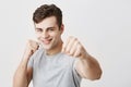 Confident muscular caucasian sportsman with dark hair dressed in gray shirt holding fists in front, going to fight and