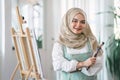 Confident muslim young female artist painting on canvas at home. Hobby and leisure concept.