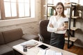 Confident nice young buisnesswoman in room. She look on camera and pose. Model hold cup of coffee. She smile.