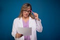 Confident nurse dressed in white coat and lilac blouse, wearing glasses with paper and pen in her hand Royalty Free Stock Photo