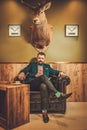 Confident old-fashioned man sitting in comfortable leather chair in wooden interior at Barber shop.