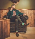 Confident old-fashioned man talking on the mobile phone in wooden interior at Barber shop.