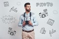 Confident photographer. Handsome young man in casual clothes is holding camera and looking away while standing against Royalty Free Stock Photo