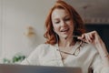 Confident pleased redhead woman concentrated in laptop computer, watches video or movie on laptop computer, enjoys friendly video