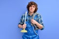 confident plumber man with curly hair in uniform holding toilet plunger isolated on blue background